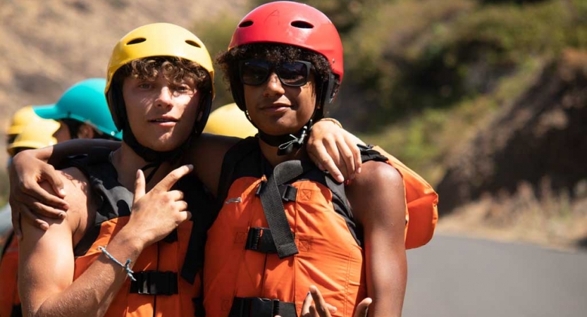 two outward bound students wearing life jackets and helmets wrap their arms around each other's shoulders and pose for the camera 